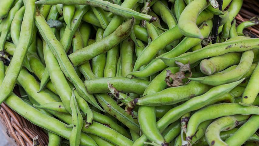 Fresh green broad beans piled in a wicker basket at a market