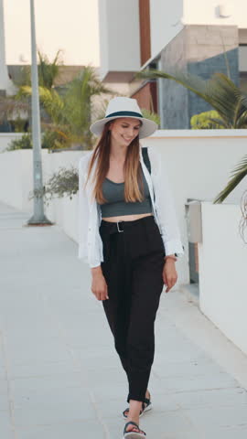 A beautiful woman with long brown hair smiles while wearing a hat and white shirt in a vertical shot