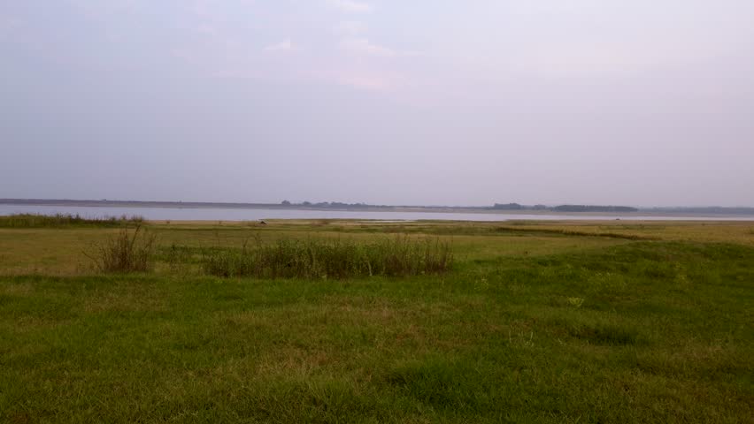Mukutmanipur Dam In Bankura District West Bengal Dynamic drone shot rising above grass fields toward wide lake under overcast evening sky.