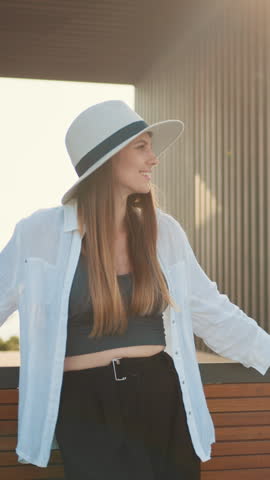 A beautiful woman with long brown hair smiles while wearing a hat and white shirt in a vertical shot