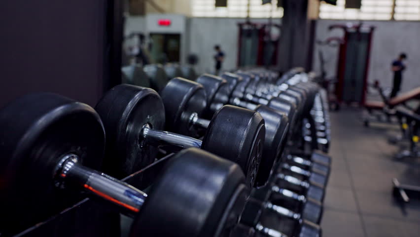 Dumbbell gym weight fitness exercise strength training workout equipment black row along rack modern indoor health club blurred background metal detail low light