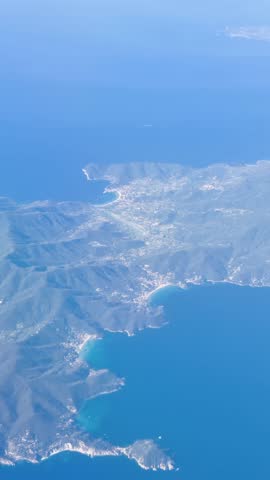 Aerial view of a rugged Italian coastline with small towns, sandy beaches, and deep blue Mediterranean waters photographed from high altitude.