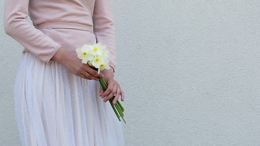 Cute woman holds a vibrant bouquet of yellow daffodils, symbolizing spring renewal. Soft pastel dress and minimalist background enhance the fresh, joyful atmosphere. Ideal for seasonal campaigns