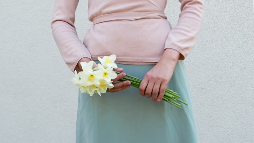 Cute woman holds a vibrant bouquet of yellow daffodils, symbolizing spring renewal. Soft pastel dress and minimalist background enhance the fresh, joyful atmosphere. Ideal for seasonal campaigns