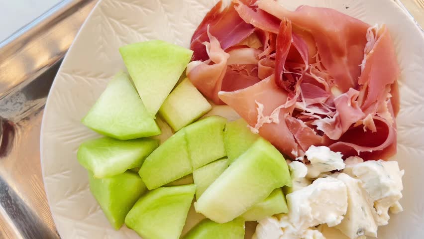 Top down view of plate with fresh green melon cubes, cured Spanish jamon slices, and blue cheese pieces served on a metal tray, Mediterranean appetizer