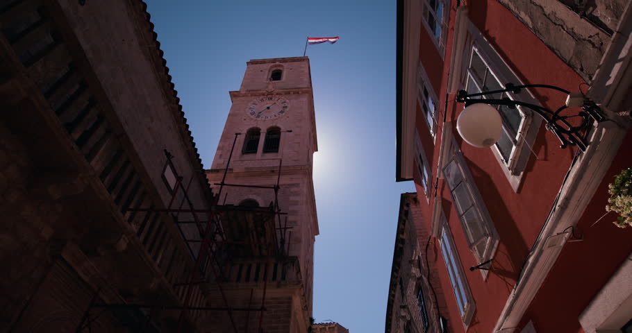 Historic stone clock tower rising above a narrow street lined with traditional buildings in the old town of Sibenik Croatia.
