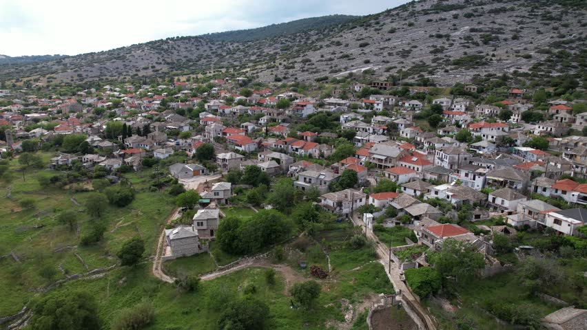 Aerial footage flying over a picturesque stone village nestled on a lush green and rocky mountainside