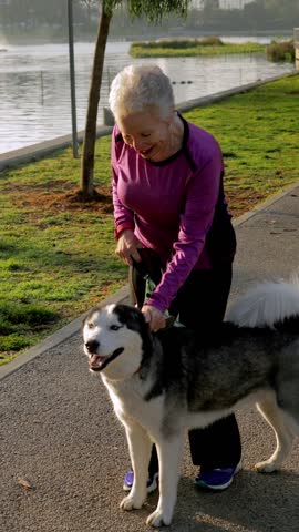 71 year old woman walking her dog in the park. Vertical video.