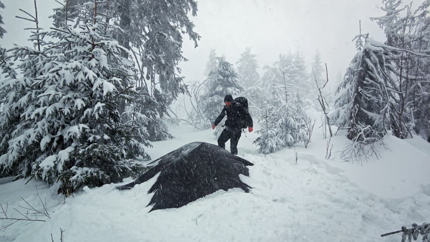Extreme blizzard storm catching a hiker near a tarp shelter on mountain peak