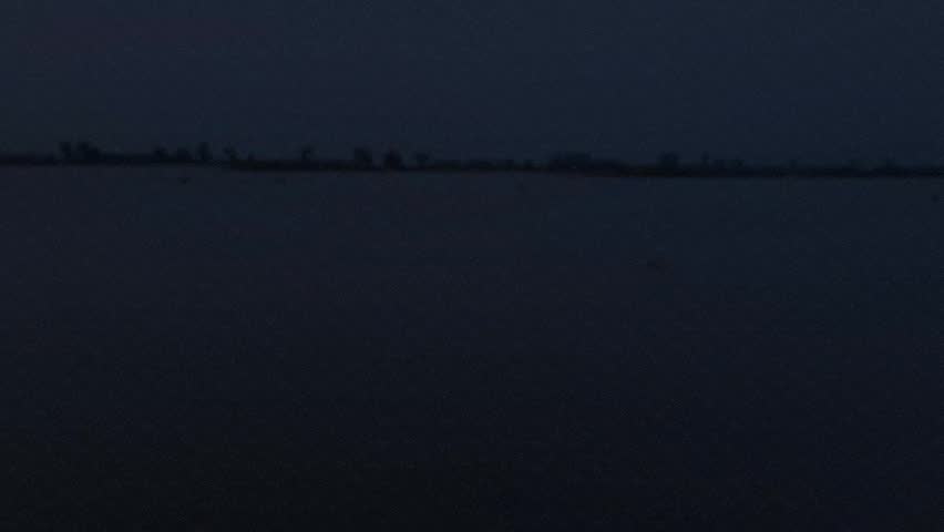 Serene river at twilight with distant horizon line under dark evening sky