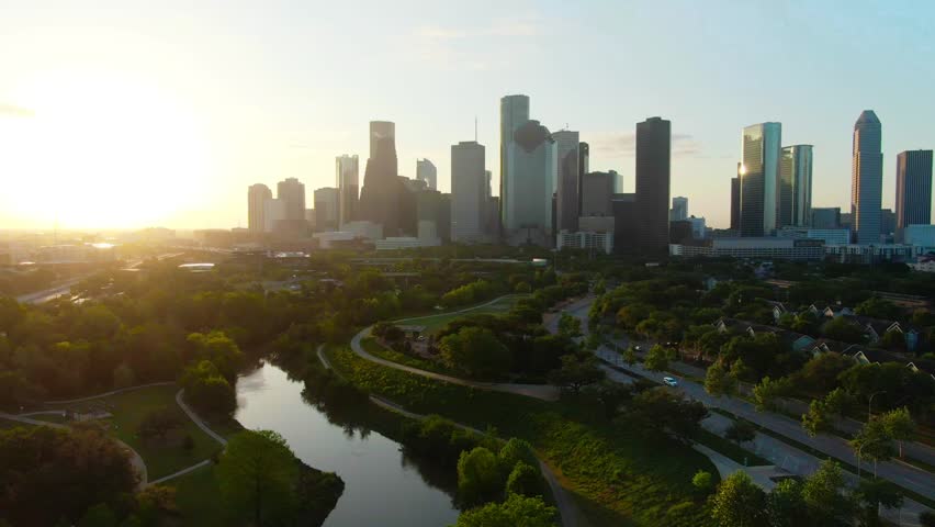 Sunrise over Houston skyline, cinematic aerial view of downtown buildings, river bend, green park, city overview, morning light, urban landscape.