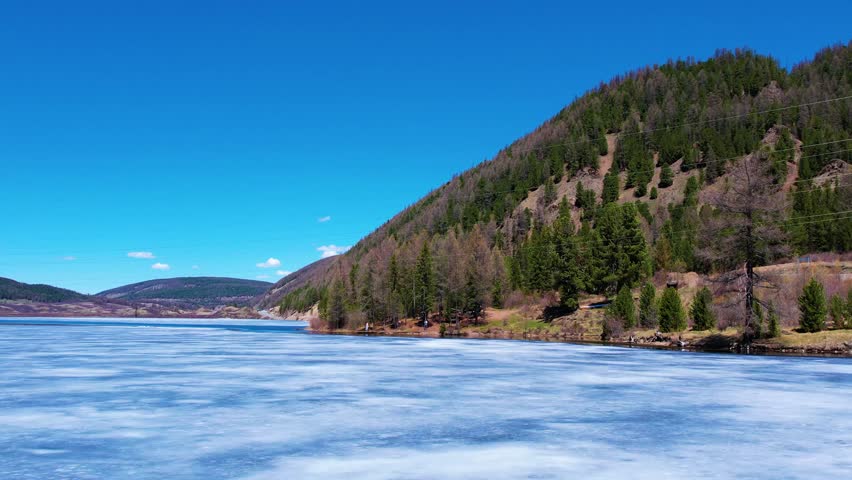 Frozen lakeshore with pine forest and sunlit mountains