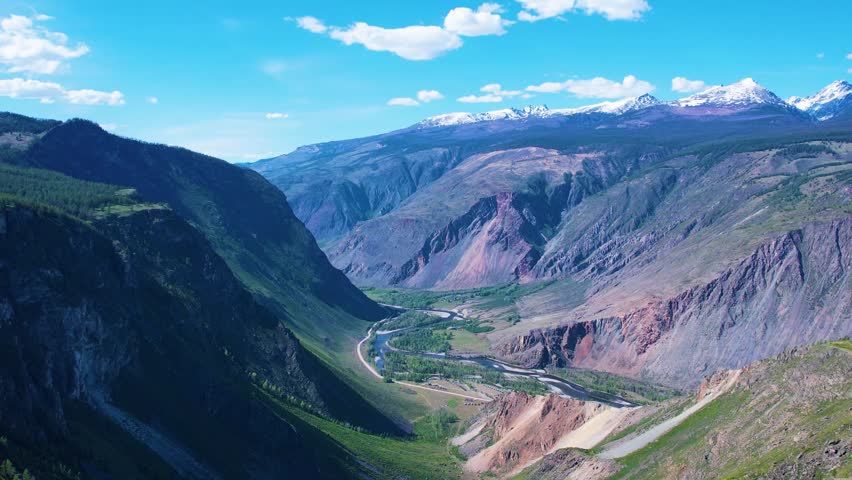 Alpine valley with river and rugged mountains under blue sky