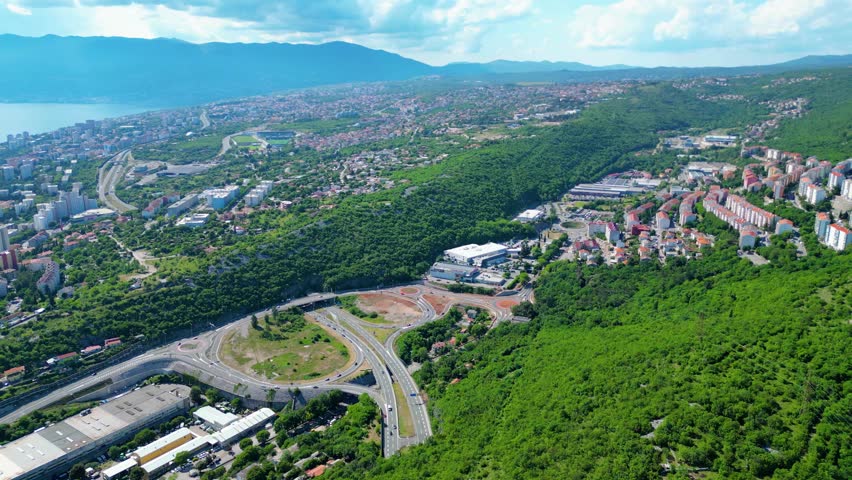 Aerial view of Rijeka, Croatia, showcasing its vibrant urban sprawl nestled amidst lush green hills, with the Adriatic Sea and mountains in the distance. Modern infrastructure connects the city.Skurinje