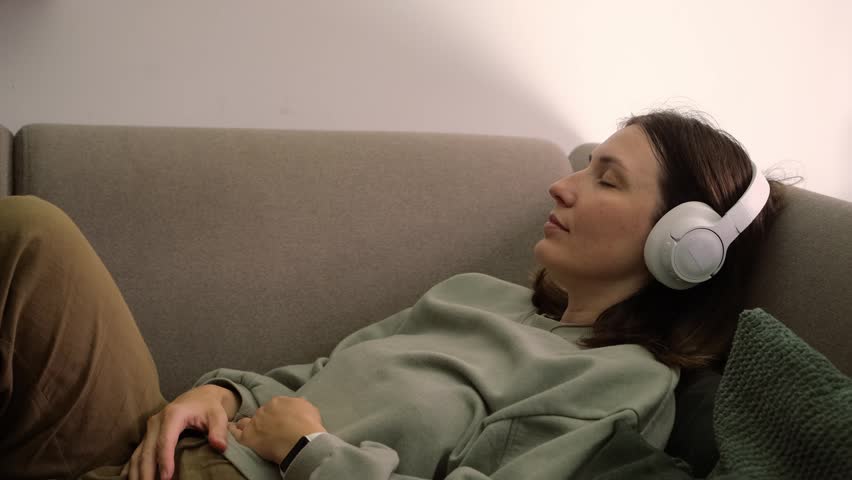 Peaceful young woman listening to music in headphones on couch