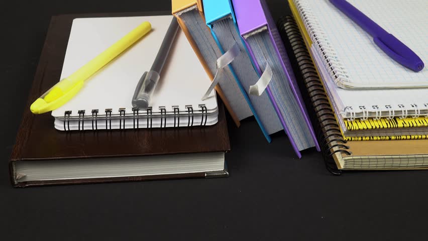 Various types of notepads and ballpoint pens lie on a black table. Sets for notations, studying, note -taking, and diary.