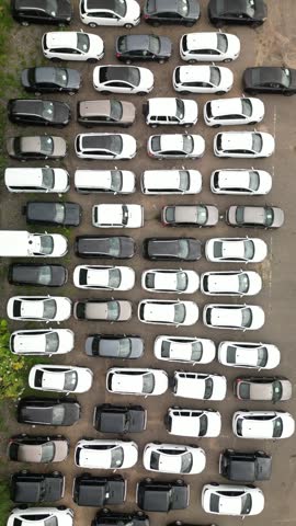 Aerial drone view of many cars parked in organized rows on an outdoor dealership lot, showing vehicle inventory, storage and automotive business from above.