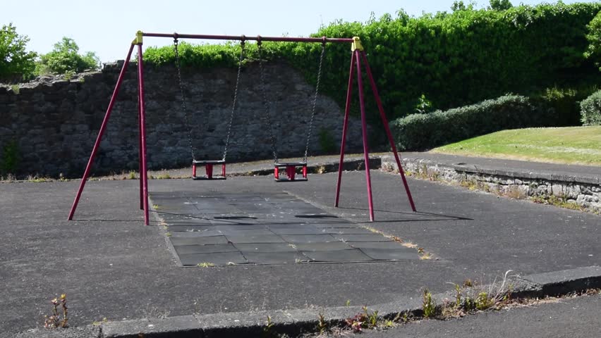 Medium wide shot of two swings in a swing park on a bright summer day with greenery in the background
