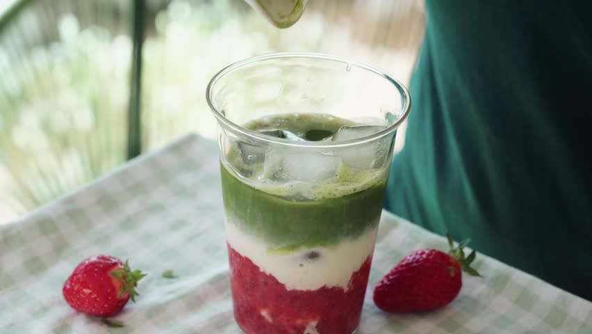 Making a layered strawberry matcha latte with fresh strawberries, milk and matcha tea. Trendy healthy beverage prepared in a glass