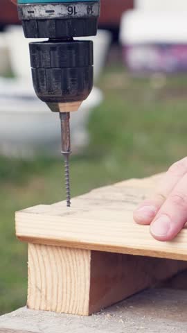 Man screwing screw in wooden plank, construction process. Vertical footage