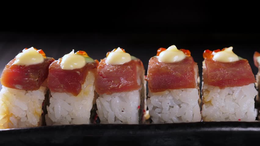 Sushi rolls with tuna on black platter and dark background. Closeup