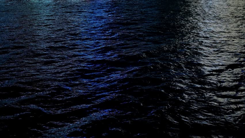 Blue and grey city lights reflecting on dark rippling ocean water at night