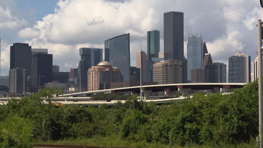 Aerial view of Houston Texas city skyline featuring skyscrapers and freeway traffic. Cinematic motion shot showing urban development and infrastructure under dynamic clouds on sunny afternoon.