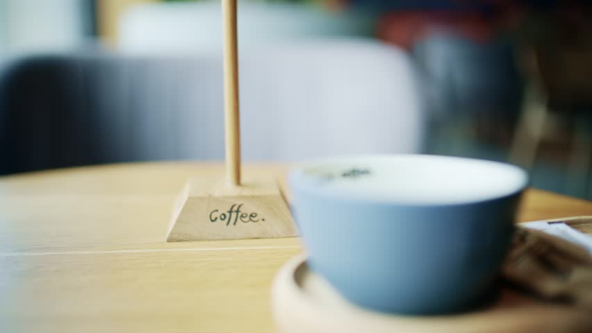 Blurred coffee cup on wooden table in cafe with focus on wooden stand with coffee lettering signpost.