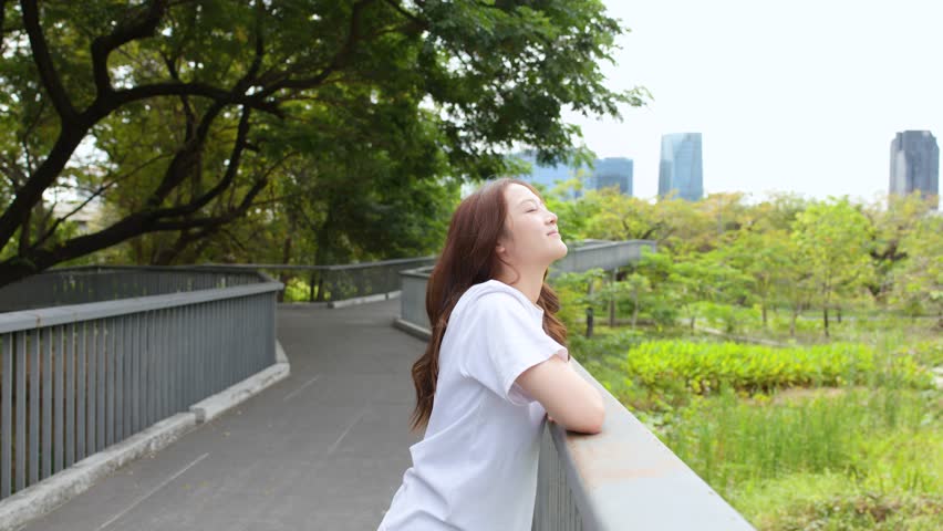 A young woman leans on a bridge railing, enjoying the breeze in a lush park