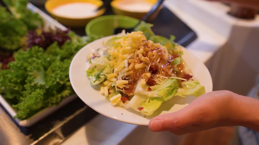 Close-up of a hand pouring dressing onto a salad plate at a restaurant buffet.
