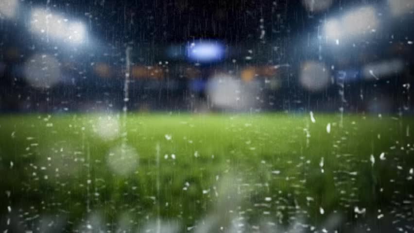 A blurry nighttime sports field with rain falling and bright stadium lights shining