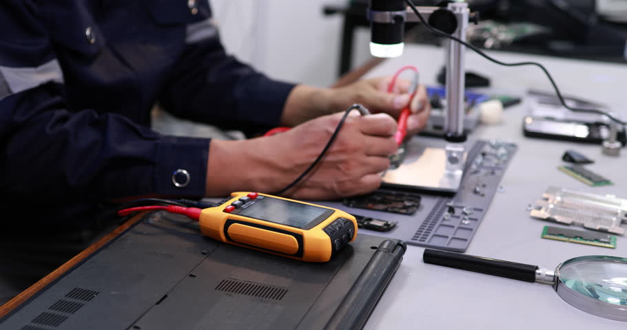 Technician repairing electronic parts on a workbench with testing tools, magnifier and circuit boards in a modern workshop.