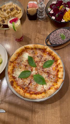 Top view of a person hand taking a slice of fresh margherita pizza from a wooden table