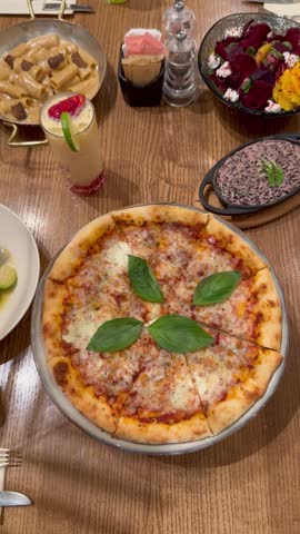 Top view of a person hand taking a slice of fresh margherita pizza from a wooden table