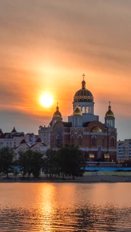 Golden sunset over Obolon Embankment in Kyiv, Ukraine. Warm evening light illuminates a riverside church and city skyline reflected in the calm waters of the Dnipro River.