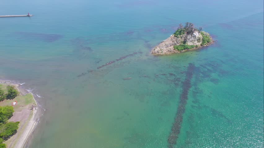 Aerial 4K view of the partially collapsed Mitsukejima Island (Battleship Island) in the clear blue sea of Noto Peninsula, Ishikawa, Japan.