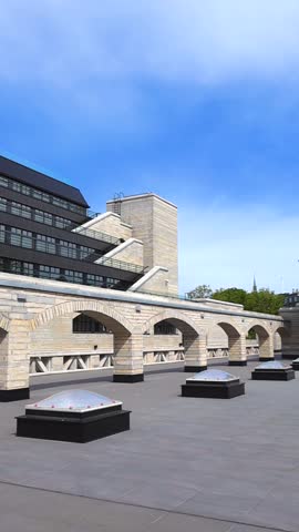 Modernist stone building facade with brutalist elements, showcasing the arches and rooftop terrace of the National Library of Estonia under a clear blue sky on a sunny summer day in Tallinn