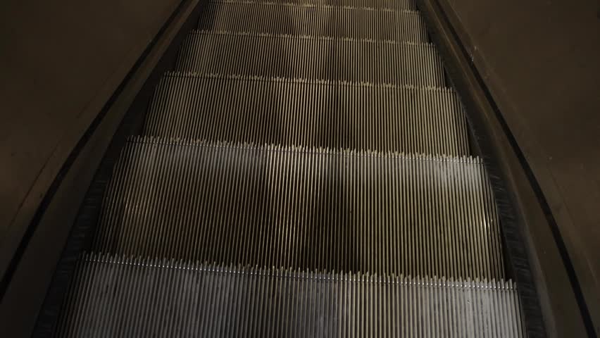 Escalator steps captured from above, illustrating the seamless transition of metal treads leading down into a shadowy underground area