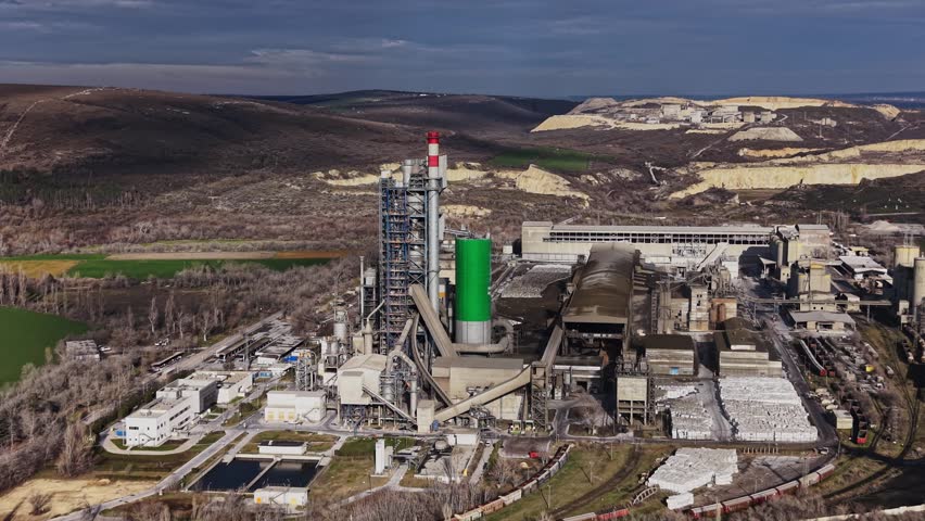 An industrial facility with a prominent green tower surrounded by hills. The sky is clear and the land features both industrial and natural elements.