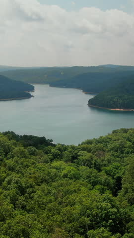 A cinematic vertical drone shot overlooking the scenic Beaver Lake in Arkansas, featuring rolling green hills and dense forest under a bright sky.