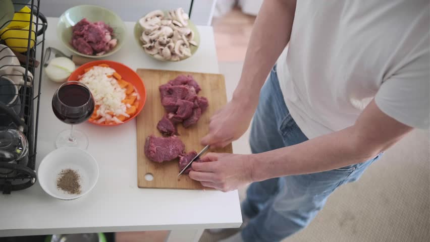 Man cutting fresh beef into cubes, preparing ingredients for cooking at home. Homemade Beef bourguignon. Part of series.