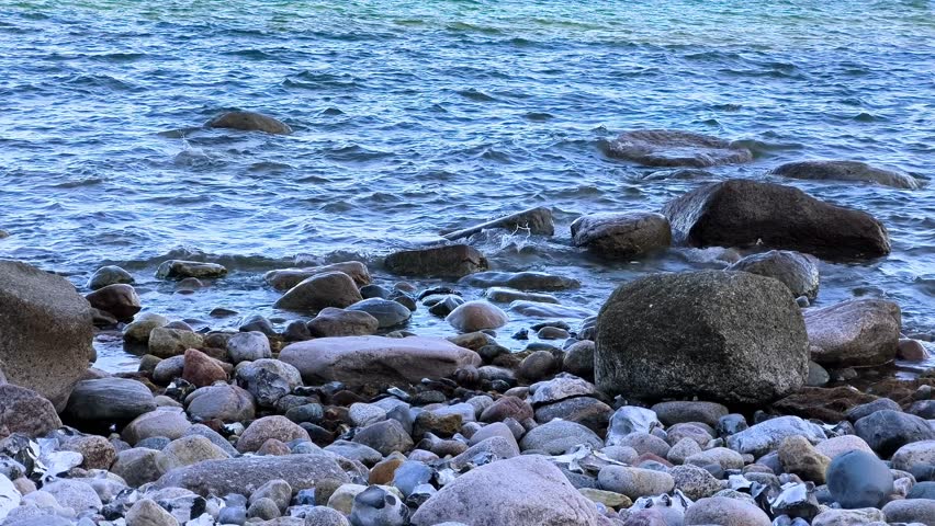 Gentle sea waves washing over rocks on a stony beach shoreline