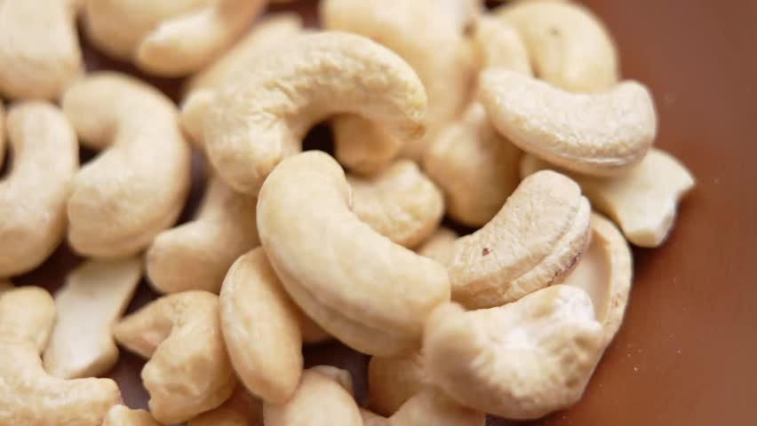 Raw cashew nuts inside a brown ceramic bowl. Hand picking a pinch of organic kernels with seeds dropping back into the plate