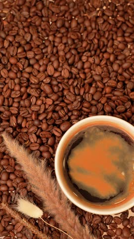 Top view of a cup of black coffee with coffee beans on a table, hand placing a small heart-shaped cookie beside it, cozy morning concept