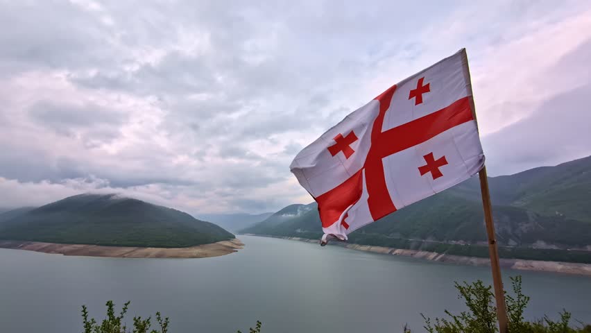 Georgia national flag waving over a river valley with cloudy mountain landscape