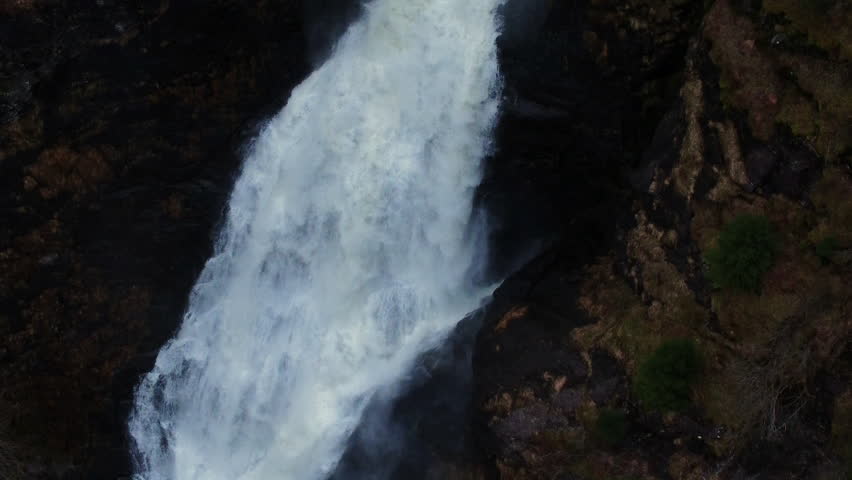 Tilt down shot of a waterfall cascading over mossy rocks in a Norwegian forest.