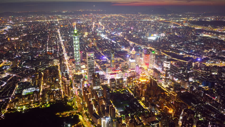 Aerial hyperlapse at night above Downtown Taipei, the vibrant capital city of Taiwan, with 101 Tower standing out amid modern skyscrapers in XinYi Commercial District and city lights dazzling under twilight sky.