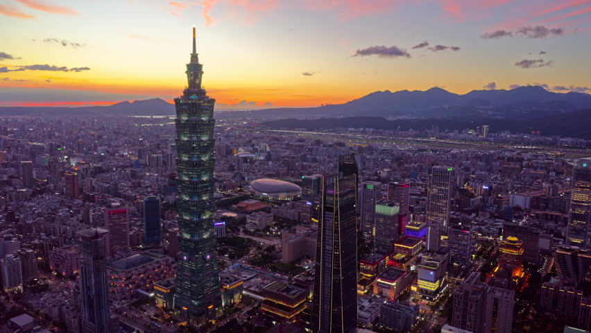 An aerial hyperlapse footage from sunset to nightfall above Downtown Taipei, the vibrant capital city of Taiwan, with 101 Tower standing out amid modern skyscrapers in XinYi Commercial District and city lights dazzling under dramatic twilight sky.