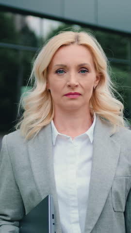 Smiling adult woman with blonde hair stand on street, looking friendly at camera. Human face, natural make up skin concept.