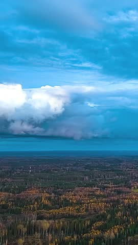 Dark storm clouds and distant rain bands move across a vast forest wilderness beneath dramatic atmospheric skies viewed from above